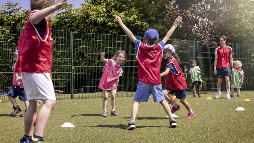 Students during a PE session having fun. Wearing red bibs coach at the back